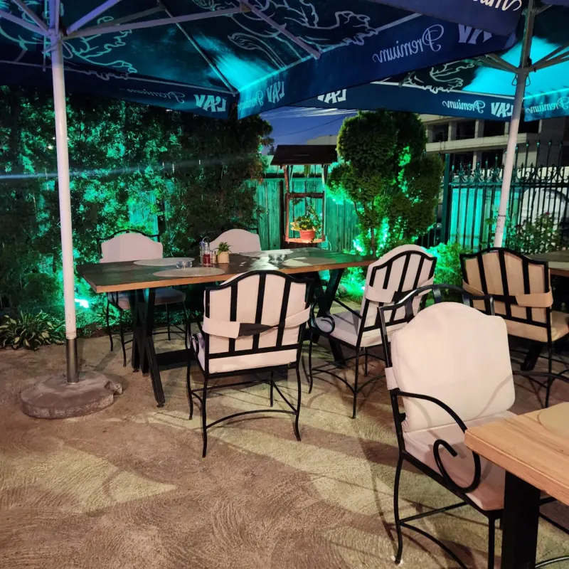 Garden tables under parasols in the evening, with green light in the greenery
